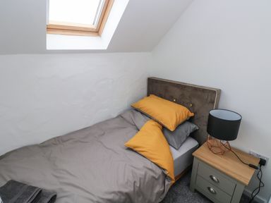 A small bedroom with a single bed an angled skylight window and a bedside table with a lamp at The Loft @ Wisteria Cottage in Saundersfoot
