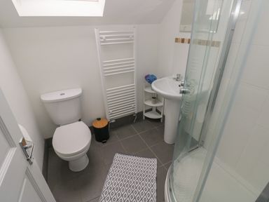 A bathroom with a toilet sink shower and towel rack with a window above at The Loft @ Wisteria Cottage in Saundersfoot