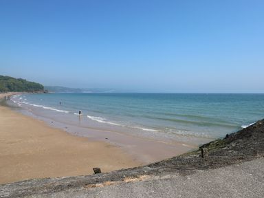 A sandy beach with a few people near the shore and the sea at The Loft @ Wisteria Cottage in Saundersfoot