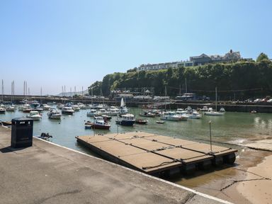 A harbor with multiple boats docked near a floating platform and a building on a hill at The Loft @ Wisteria Cottage in Saundersfoot