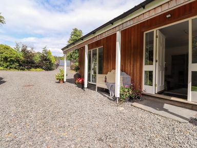 A gravel driveway alongside a wooden house with white pillars and an open door at Watersong Coniston