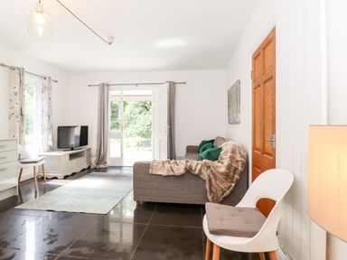 A living room with a sofa and throw blanket a chair a television and doors leading outside at Watersong in Coniston