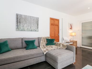 A living room with a gray sectional sofa green pillows a wooden door a white chair a lamp and wall art at Watersong in Coniston