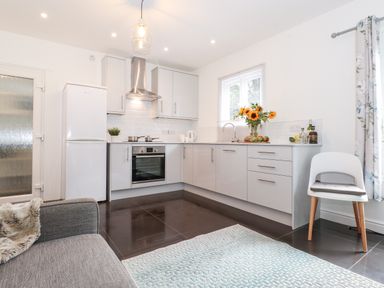 A kitchen with white cabinets a refrigerator an oven a chair and a grey sofa at Watersong in Coniston