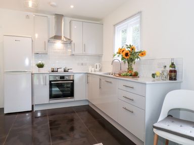 A kitchen with white cabinets a refrigerator an oven a sink a chair and sunflowers in a vase on the counter at Watersong in Coniston
