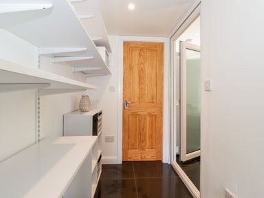 A narrow room with white shelves along one wall a wooden door and a glass door with frosted glass at Watersong Coniston