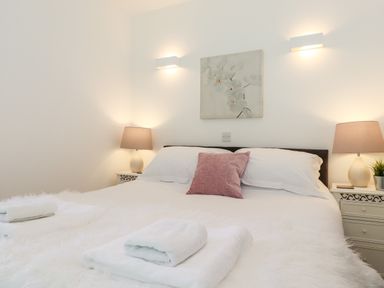 A bedroom with a bed with white bedding and a pink pillow with lamps on bedside tables at Watersong in Coniston