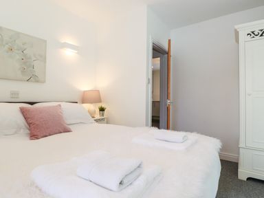 A bedroom with a bed a nightstand with a lamp and plant an open door and a white wardrobe at Watersong in Coniston