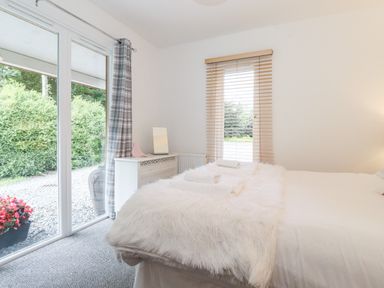 A bedroom with a bed covered with white fur and towels a dresser with a mirror and a window with blinds next to sliding glass doors at Watersong in Coniston