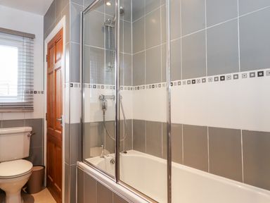 A bathroom with a bathtub shower combination and a toilet near a wooden door at Watersong in Coniston