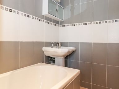A bathroom with a bathtub a pedestal sink and a mirrored cabinet on tiled walls at Watersong in Coniston