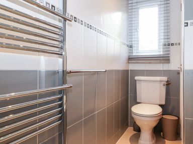 A bathroom with a toilet, a small window with blinds, a wall-mounted towel rail, and a small trash bin at Watersong in Coniston