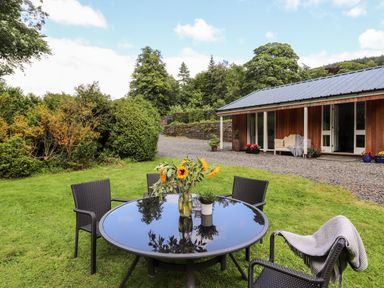 A garden with a round glass table and four chairs with sunflowers on the table at Watersong in Coniston
