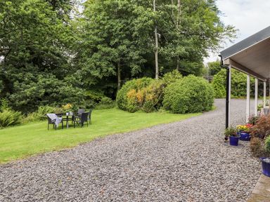 A garden with chairs and a table on grass next to a gravel driveway and bushes at Watersong in Coniston