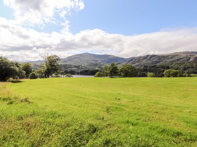 A grassy field with trees hills and a lake in the background at Watersong in Coniston
