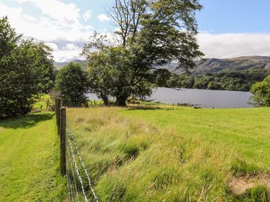 A grassy field with a wire fence trees and a lake with hills in the background at Watersong in Coniston