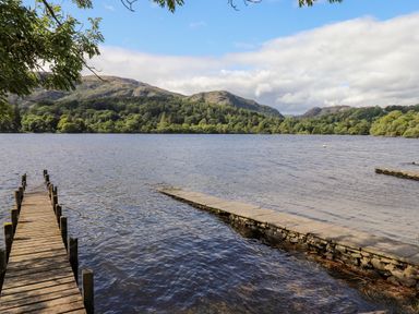 A wooden jetty and stone pier on a lake with hills and trees in the background at Watersong in Coniston