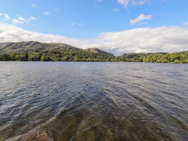 A lake with forested hills and mountains in the background under a partly cloudy sky at Watersong in Coniston