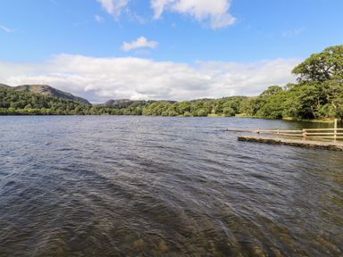 A lake with hills and trees in the background and a wooden dock at Watersong in Coniston