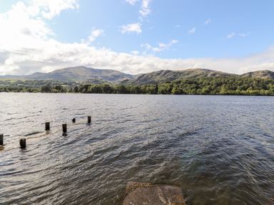 A lake with wooden posts in the water and hills in the background at Watersong in Coniston