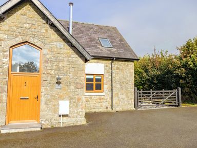 Stone house with wooden door and window next to a black wooden gate at School Lodge in Llandeilo