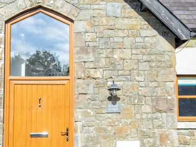 A wooden door and window on a stone wall with a lamp and a sign that reads School Lodge at School Lodge in Llandeilo
