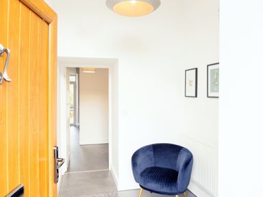 A hallway with a blue armchair next to a radiator and two framed pictures on the wall at School Lodge in Llandeilo