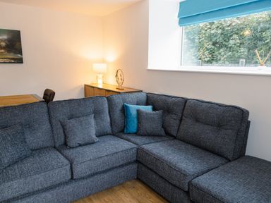 A living room with a gray sectional sofa and cushions next to a window and wooden sideboard with a lamp at School Lodge in Llandeilo