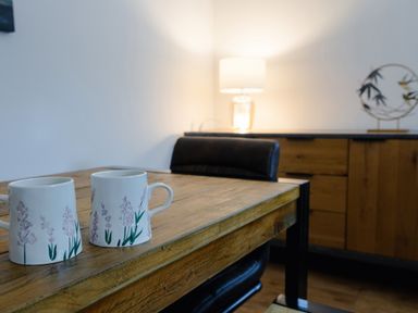 A wooden table with two floral mugs and a black chair in a room with a lamp and wooden cabinet at School Lodge in Llandeilo
