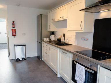 A kitchen with white cabinets a stainless steel refrigerator a black sink an oven with a towel and a trash bin at School Lodge in Llandeilo