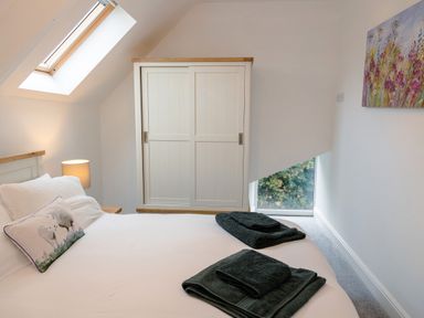A bedroom with a bed folded towels a bedside lamp a wardrobe and a painting at School Lodge in Llandeilo
