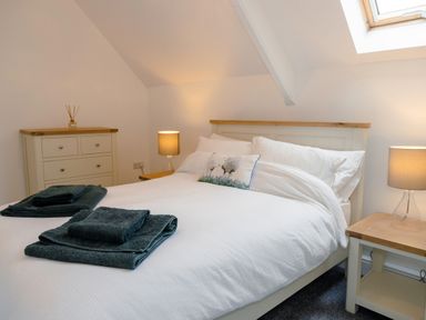 A bedroom with a bed white bedding navy towels bedside tables lamps and a chest of drawers at School Lodge in Llandeilo