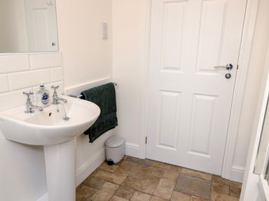 A bathroom with a white pedestal sink with soap a towel rack with a green towel a small white trash bin and a closed white door at School Lodge in Llandeilo