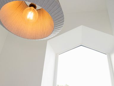 A light bulb with a shade hanging from the ceiling near a window with white walls at School Lodge in Llandeilo