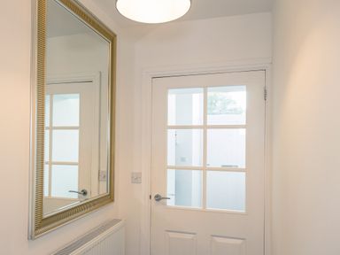 A small entryway with a white door with glass panes a large wall mirror and a radiator at School Lodge in Llandeilo