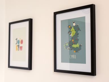 Two framed pictures on a wall one with colorful letters and one with a map labeled Cymru at School Lodge in Llandeilo
