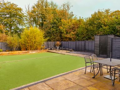A backyard with a green lawn area patio with a table and chairs a wooden shed and trees along a black fence at School Lodge in Llandeilo