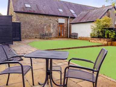 An outdoor patio with metal table and chairs and artificial grass at School Lodge in Llandeilo