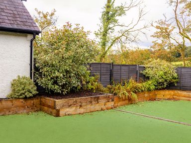 A garden area with wooden planters along a black fence and green artificial grass at School Lodge in Llandeilo