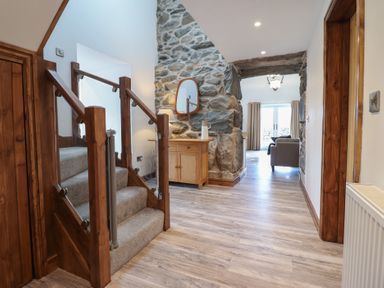 A hallway with wooden stairs carpeted with grey and a wooden cabinet with mirror near a stone wall at Gaerau Bach in Llanaber