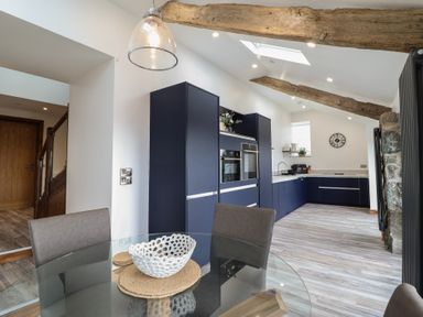 A kitchen with blue cabinets a glass dining table with a white bowl and wooden placemats at Gaerau Bach in Llanaber