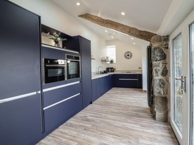 A kitchen with blue cabinets wooden beam and stone wall at Gaerau Bach in Llanaber