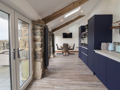 A kitchen and dining area with blue cabinets wooden beams and glass doors at Gaerau Bach in Llanaber
