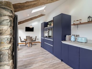 A kitchen area with blue cabinets and appliances next to a dining area with a glass table and four chairs at Gaerau Bach in Llanaber