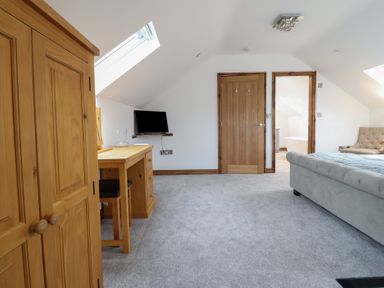 A bedroom with a wooden wardrobe a desk with a chair and a small wall-mounted television at Gaerau Bach in Llanaber