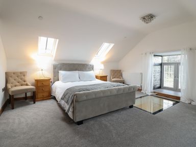 A bedroom with a bed, two chairs, nightstands with lamps, skylights, and a glass floor panel at Gaerau Bach in Llanaber
