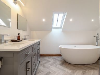 A bathroom with a freestanding bathtub a gray vanity with two sinks two mirrors and a skylight at Gaerau Bach in Llanaber