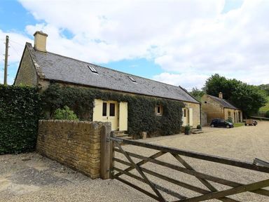 A stone building with ivy on the walls and a wooden gate in front at The Granary in Bourton-On-The-Water