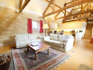 A living room with two patterned sofas a wooden coffee table and a rug under exposed wooden beams at The Granary in Bourton-On-The-Water
