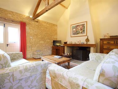 A living room with floral patterned sofas a wooden coffee table a fireplace and stone walls at The Granary in Bourton-On-The-Water
